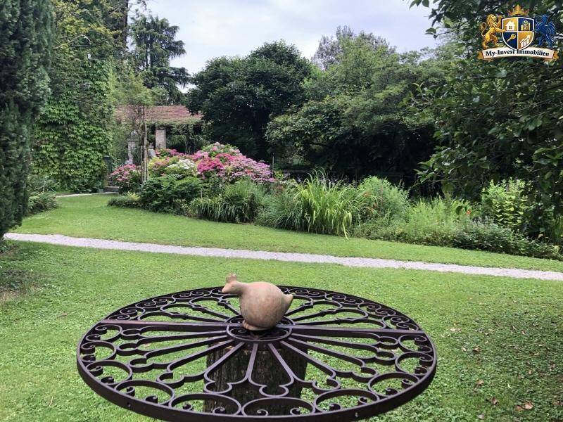Idyllischer Gartenbereich mit üppigen Blumenbeeten, Rasen und einem dekorativen Eisentisch.