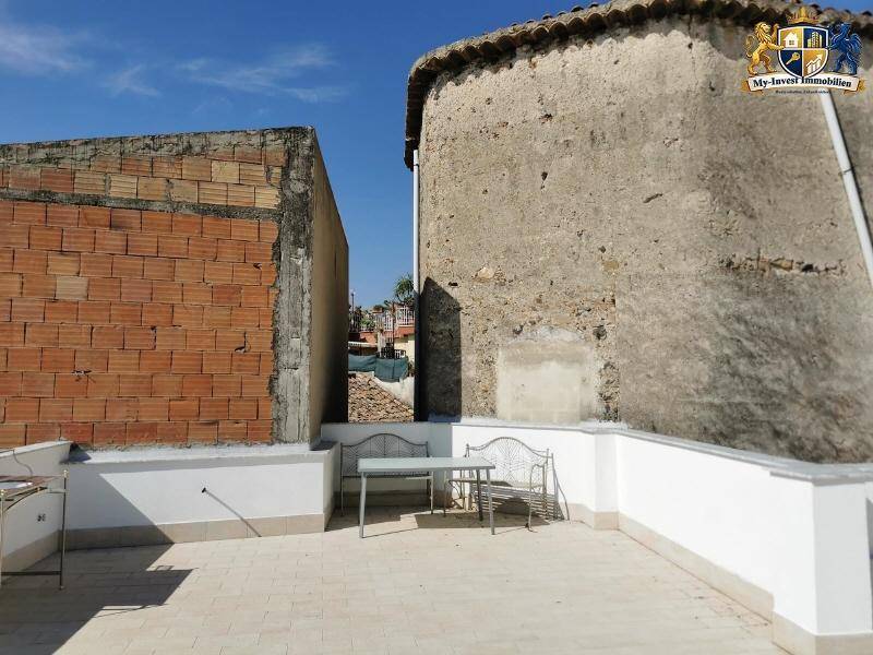 Dachterrasse mit einfacher Sitzgelegenheit und Blick auf die charakteristischen alten Gebäude der Umgebung.