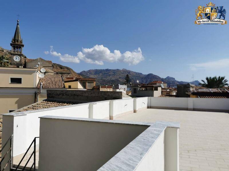 Weitläufige Dachterrasse mit Panoramablick auf einen Kirchturm und die beeindruckende Berglandschaft im Hintergrund.