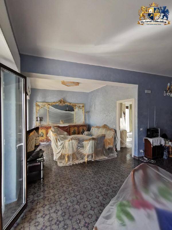 Innenraum mit blauen Wänden, gefliestem Boden und abgedeckten Möbeln, bereit für die Renovierung oder den Umzug.