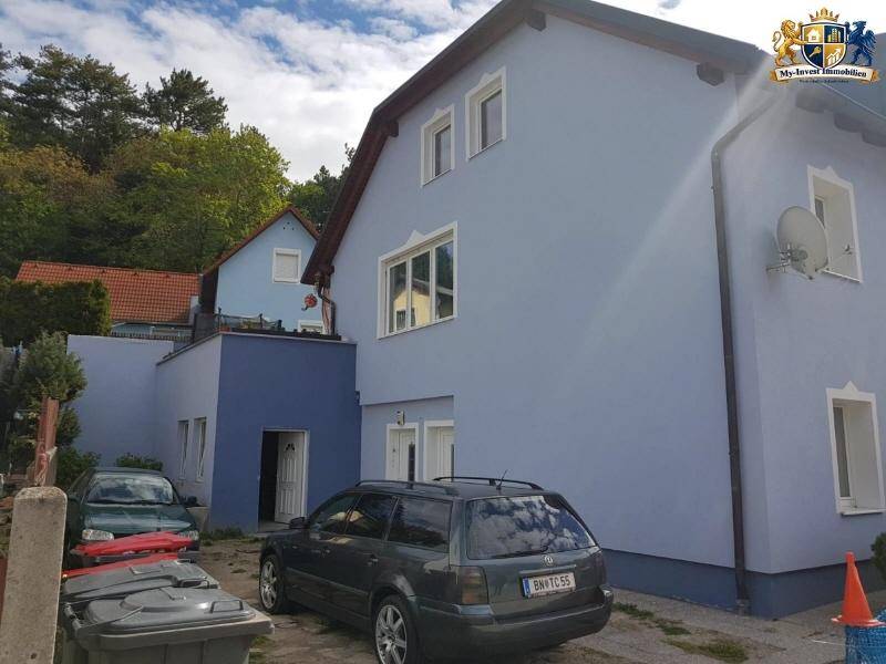 Seitenansicht des Hauses mit Eingangsbereich, geparktem Auto und umgebender grüner Landschaft.