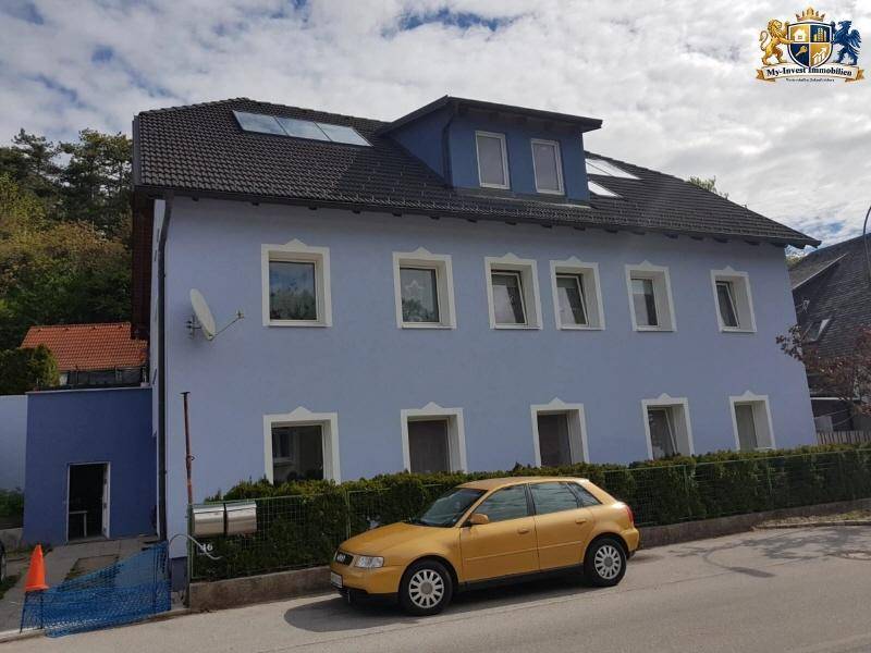 Seitenansicht des Wohnhauses mit blauer Fassade, Dachfenstern und Satellitenschüssel an der Wand.