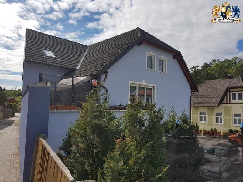 Seitliche Ansicht des Hauses mit kleinem Balkon und Trampolin, umgeben von Bäumen.