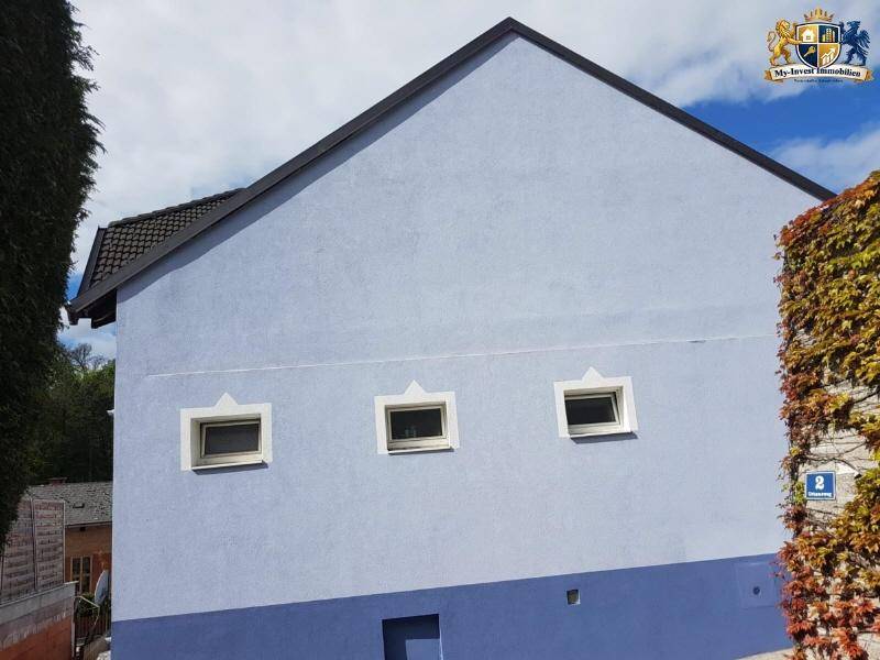 Seitenfassade des Hauses mit drei kleinen Fenstern und Kletterpflanzen an der Wand.