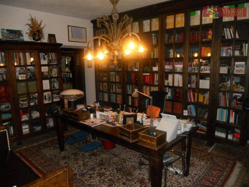 Großes Arbeitszimmer mit raumhohen Bücherregalen, Schreibtisch und opulentem Kronleuchter.