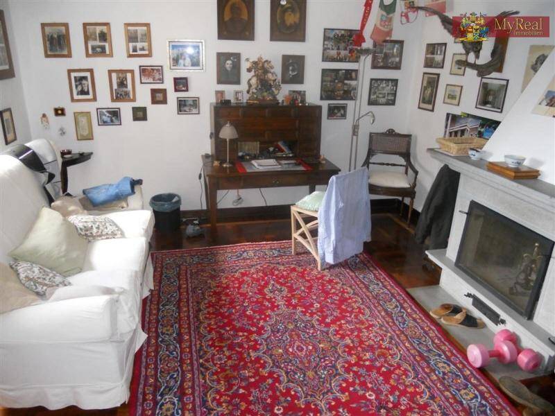 Gemütliches Wohnzimmer mit Kamin, weißem Sofa und vielen Familienfotos an der Wand.