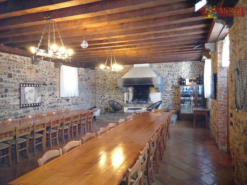 Großer Speisesaal mit langen Holztischen, Steinfliesenboden und einem imposanten Kamin.