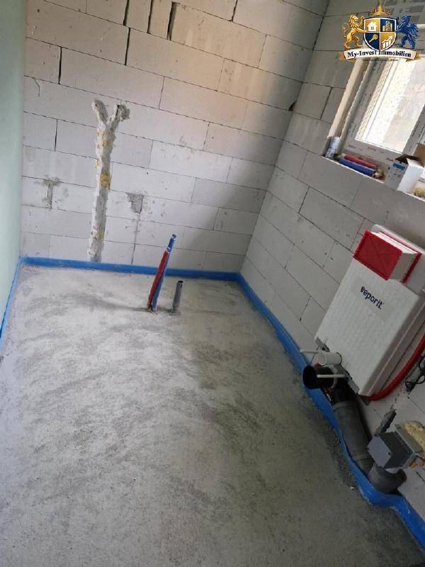 Unfertiges Badezimmer im Rohbau mit Fenster und vorbereiteten Sanitäranschlüssen.