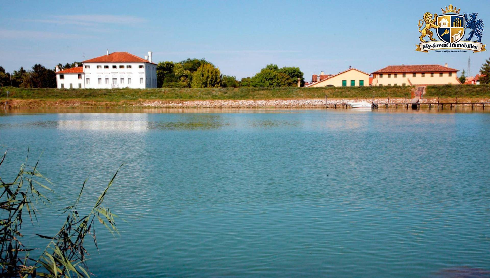 Malerischer Blick über das ruhige Wasser auf die historische Villa und die umliegenden Gebäude.