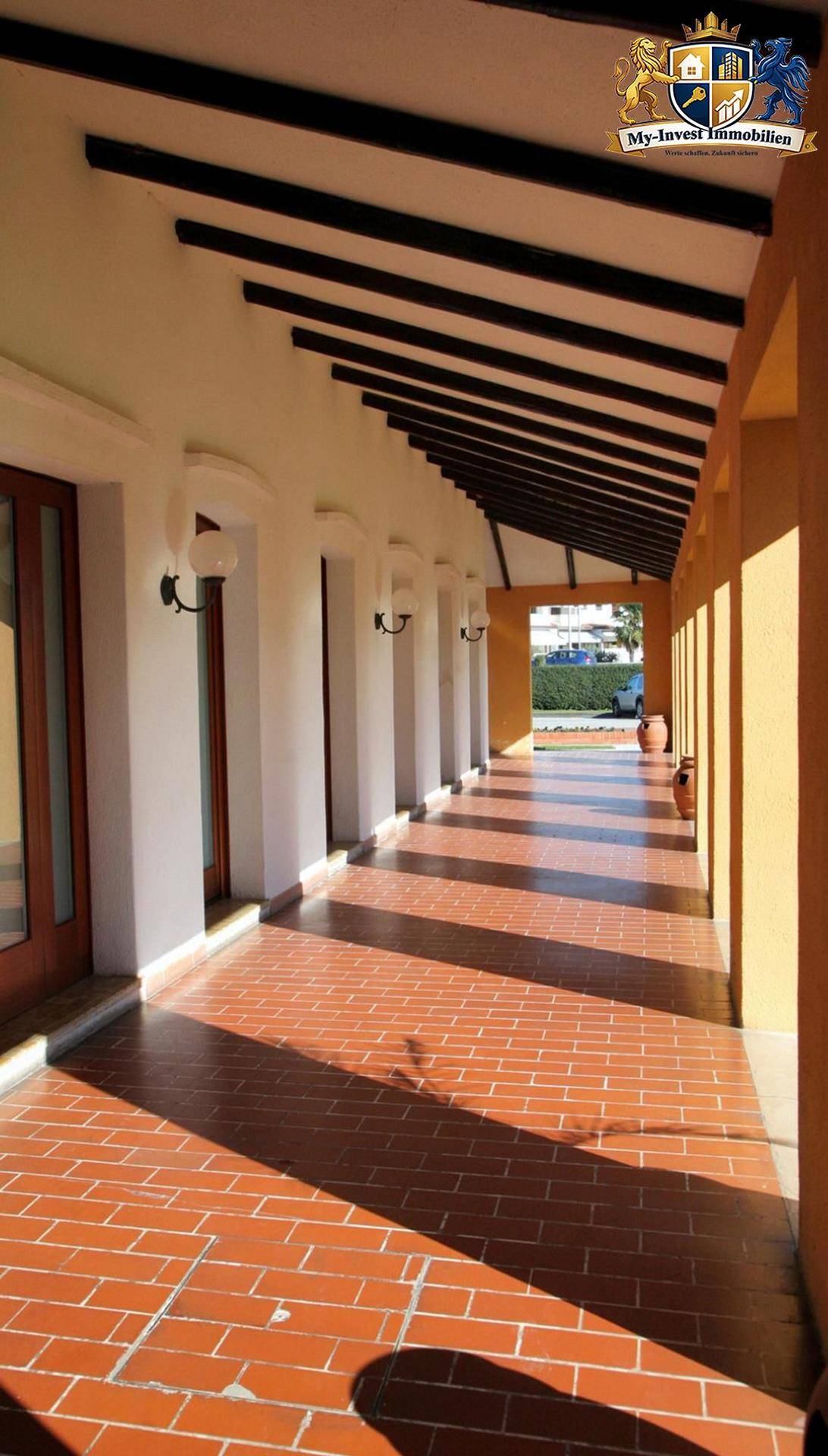 Lange, überdachte Loggia mit Terrakotta-Fliesenboden und Holzbalken, die zum Garten führt.