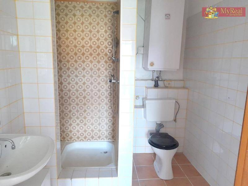 Badezimmer mit Dusche, WC und Waschbecken, ausgestattet mit älteren Fliesen und einem Boiler.