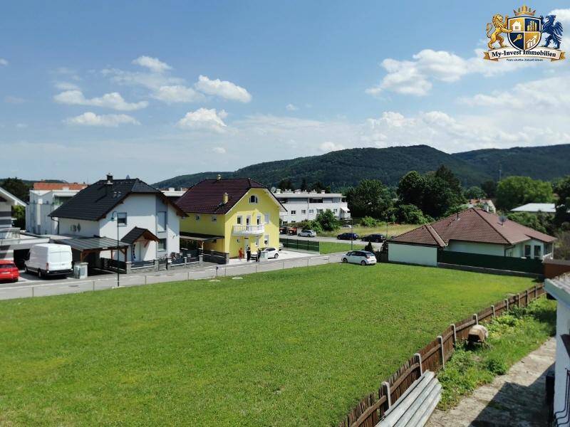 Weitläufiger Blick über grüne Wiesen und Wohnhäuser in ländlicher Umgebung mit Bergen im Hintergrund.