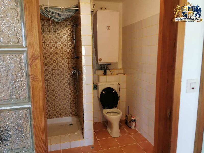 Badezimmer mit Dusche, WC und Glasbausteinen, ausgestattet mit älteren Fliesen und einem Boiler.
