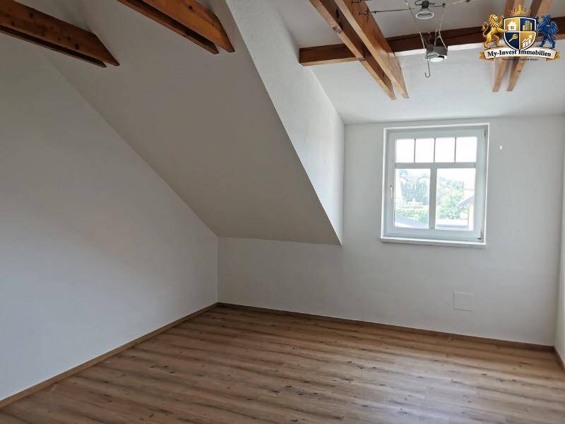 Gemütliches Schlafzimmer im Dachgeschoss mit Holzboden, Dachschräge und einem Fenster.