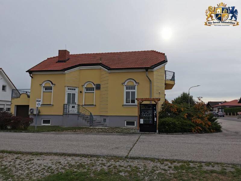 Ansicht des gelben Wohnhauses mit rotem Dach und Eingangsbereich von der Straße aus.