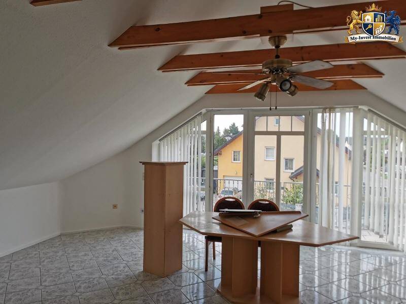 Helles Zimmer im Dachgeschoss mit großen Fenstern, Fliesenboden und sichtbaren Holzbalken.