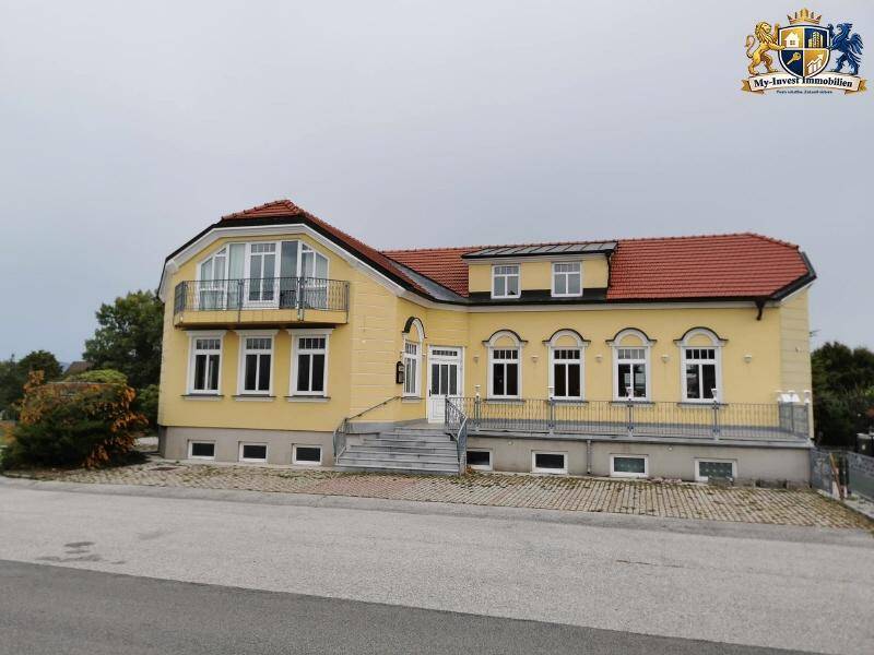 Vorderansicht des gelben Wohnhauses mit rotem Dach und Balkon im Obergeschoss.