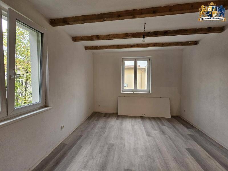 Unmöblierter Raum mit Holzbalken an der Decke und hellgrauem Laminatboden.