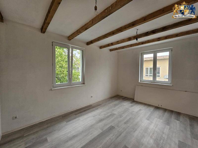 Heller Raum mit sichtbaren Holzbalken an der Decke und modernem Laminatboden.