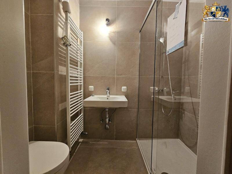 Modernes Badezimmer mit ebenerdiger Dusche, Einzelwaschbecken und beheiztem Handtuchhalter.