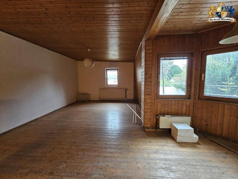 Geräumiger Wohnbereich mit Holzverkleidung an Wänden und Decke sowie Holzboden.