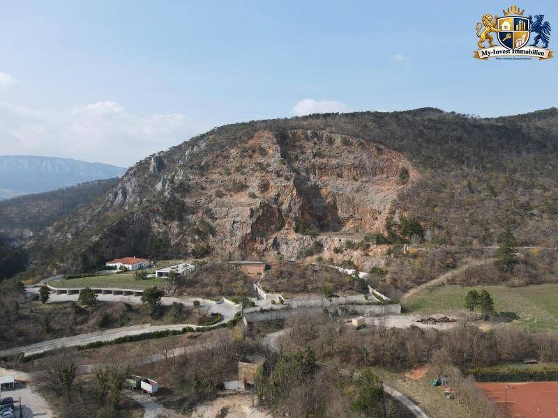 Panoramablick auf eine beeindruckende Felswand und die umliegende bergige Landschaft mit vereinzelten Gebäuden.