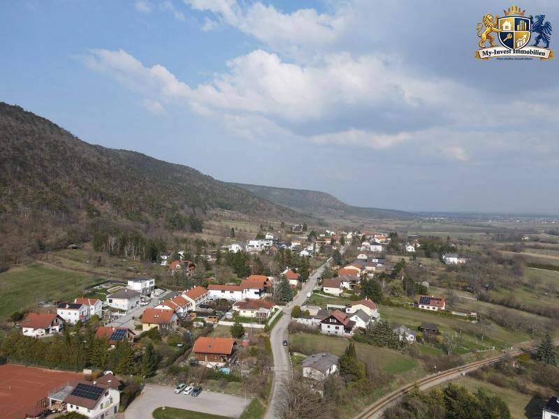 Weitläufige Luftaufnahme eines malerischen Dorfes in einer Talregion mit grünen Hügeln und Bergen.
