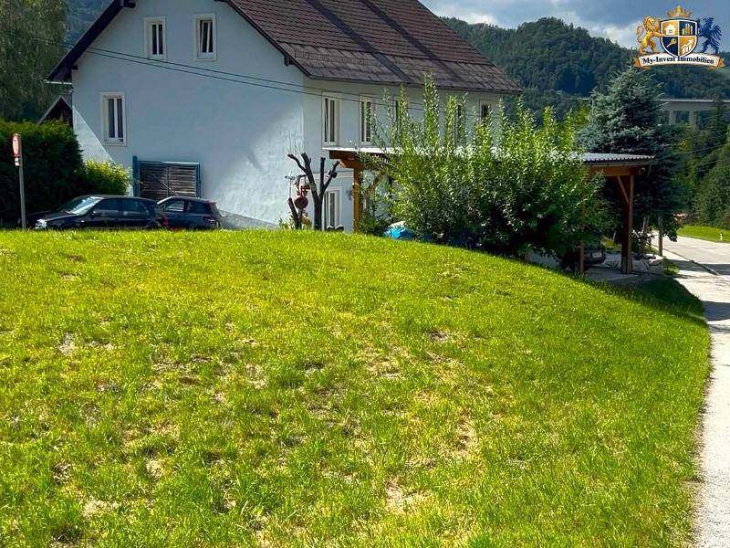 Ansicht eines traditionellen Hauses mit hellblauer Fassade und einem grünen Rasen im Vordergrund.