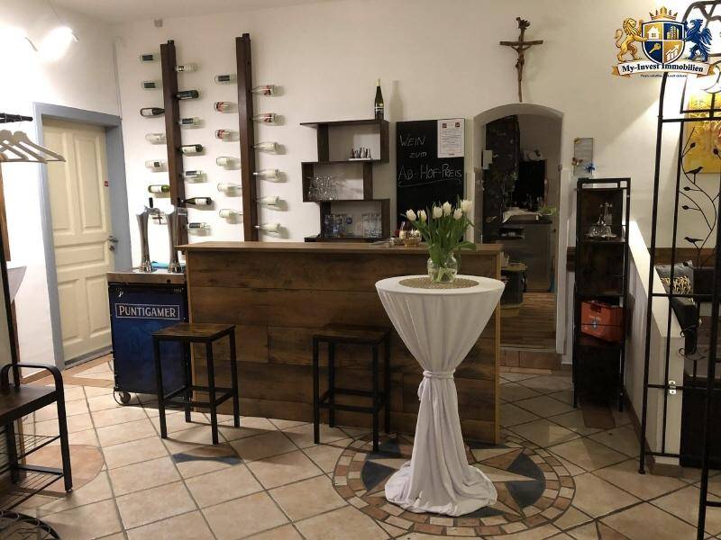 Barbereich mit Holztresen, Weinregal und einem Stehtisch, dekoriert mit frischen Blumen für eine einladende Atmosphäre.