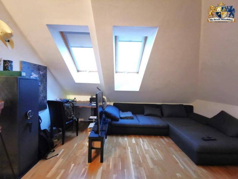 Gemütlicher Wohnbereich mit großem Sofa, Fernseher und zwei hellen Dachfenstern im Dachgeschoss.
