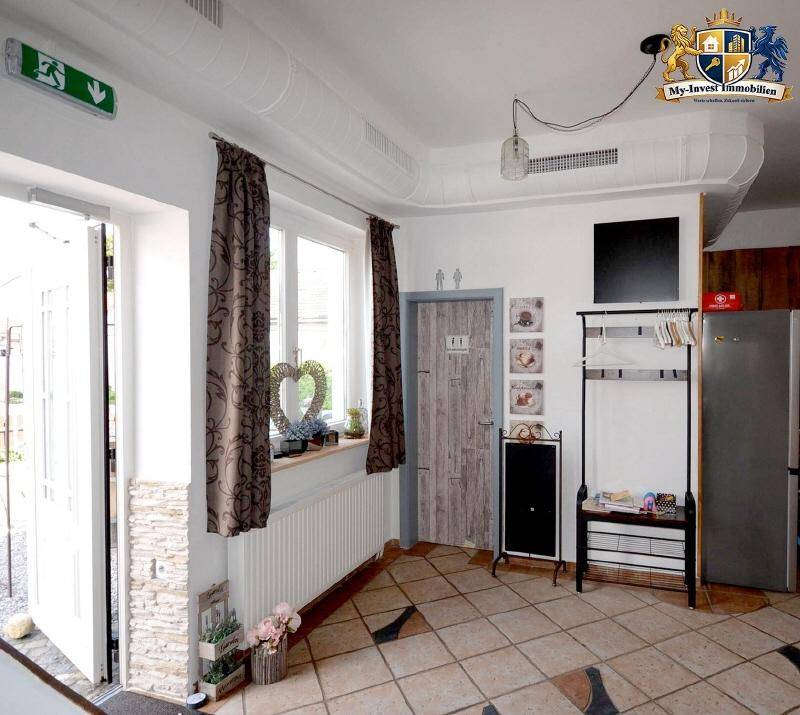 Eingangsbereich mit Fenster, Heizkörper, Garderobe und einer Tür mit rustikalem Design, gut beleuchtet.