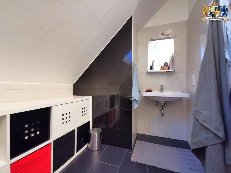 Modernes Badezimmer mit Waschbecken, Spiegel und praktischen Ablagemöglichkeiten unter der Dachschräge.