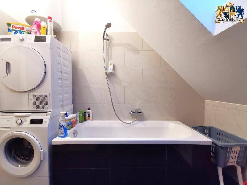 Badezimmer mit Badewanne und praktischer Waschmaschine sowie Trockner unter der Dachschräge.