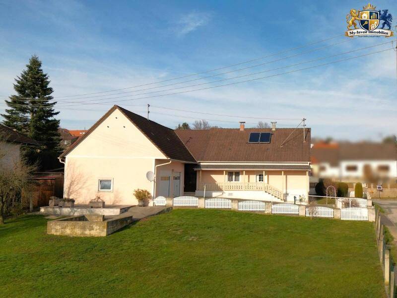 Seitenansicht des Hauses mit großem Rasenbereich, gepflasterter Terrasse und weißem Zaun.
