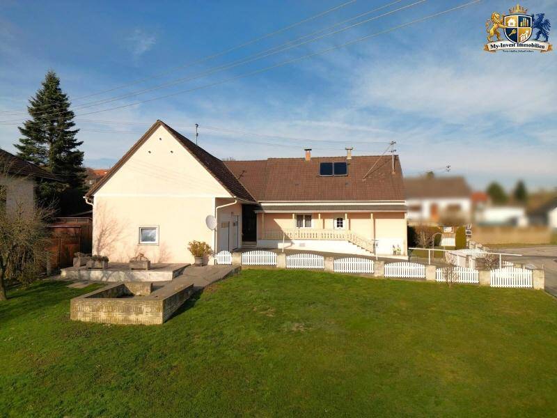 Seitenansicht des Hauses mit großem Rasenbereich, gepflasterter Terrasse und weißem Zaun.