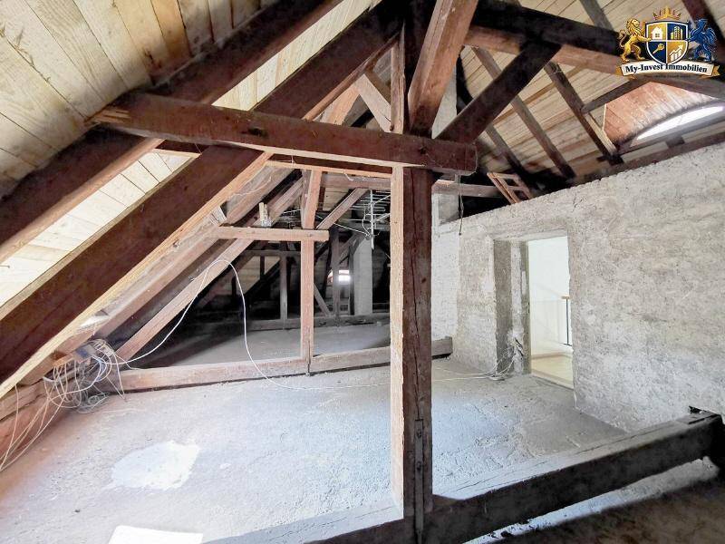 Dachboden mit sichtbarem Holzgebälk und offenem Zugang zu einem weiteren Raum, ideal für Ausbau.