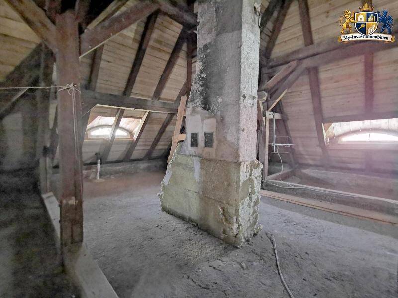 Geräumiger Dachboden mit freiliegenden Holzbalken und einem massiven Pfeiler, ideal für Umbau.