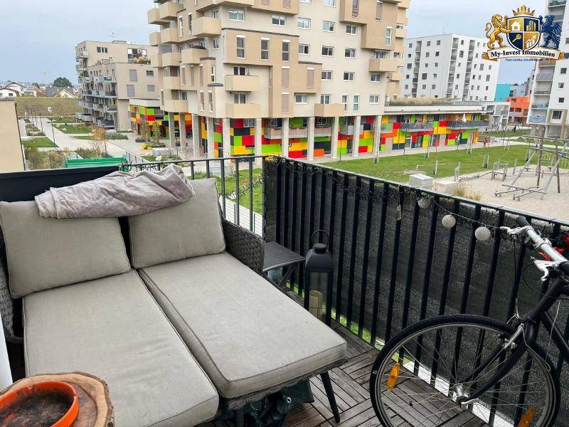 Gemütlicher Balkon mit Liegemöbeln und Blick auf einen Spielplatz und die umliegende Bebauung.