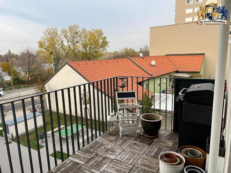 Balkon mit Holzboden, Grill und Blick auf die umliegenden Gebäude und herbstliche Bäume.