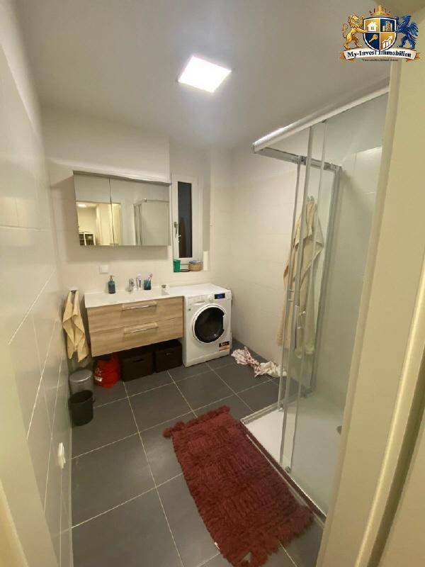 Modernes Badezimmer mit Dusche, Waschbecken und integrierter Waschmaschine, hell gefliest.