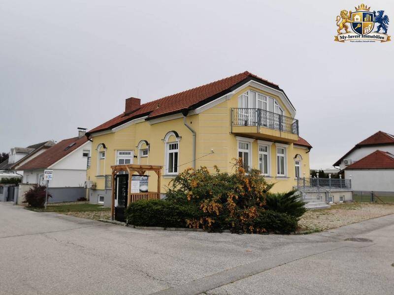 Seitenansicht des charmanten gelben Hauses mit rotem Dach und üppiger Bepflanzung im Vorgarten.