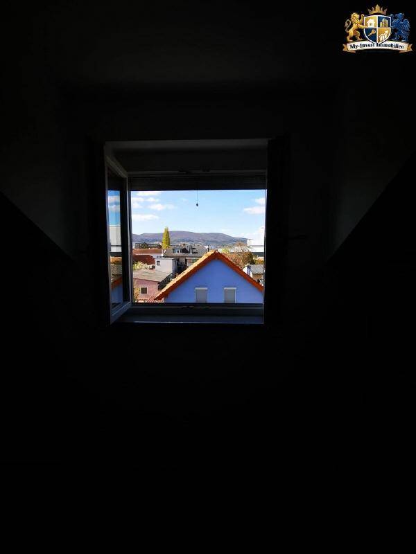 Kleines Fenster in einem dunklen Raum mit Blick auf ein blaues Dach und die umliegende Landschaft.