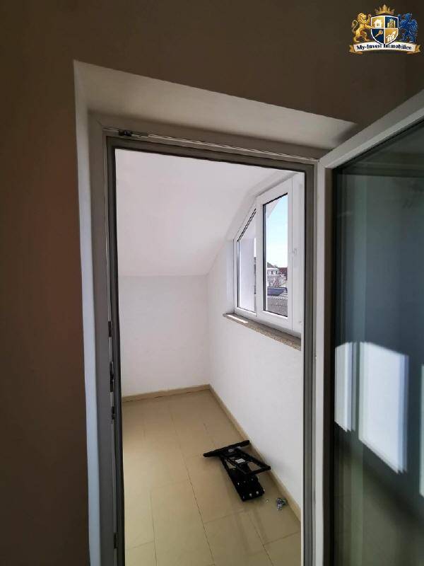 Heller Balkonbereich mit Dachschräge und Fenster, der einen Blick nach draußen ermöglicht.