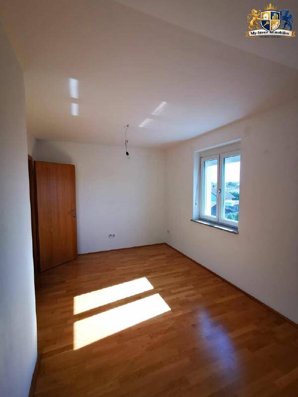 Helles Schlafzimmer mit Holzparkettboden und einem Fenster, das viel Tageslicht hereinlässt.