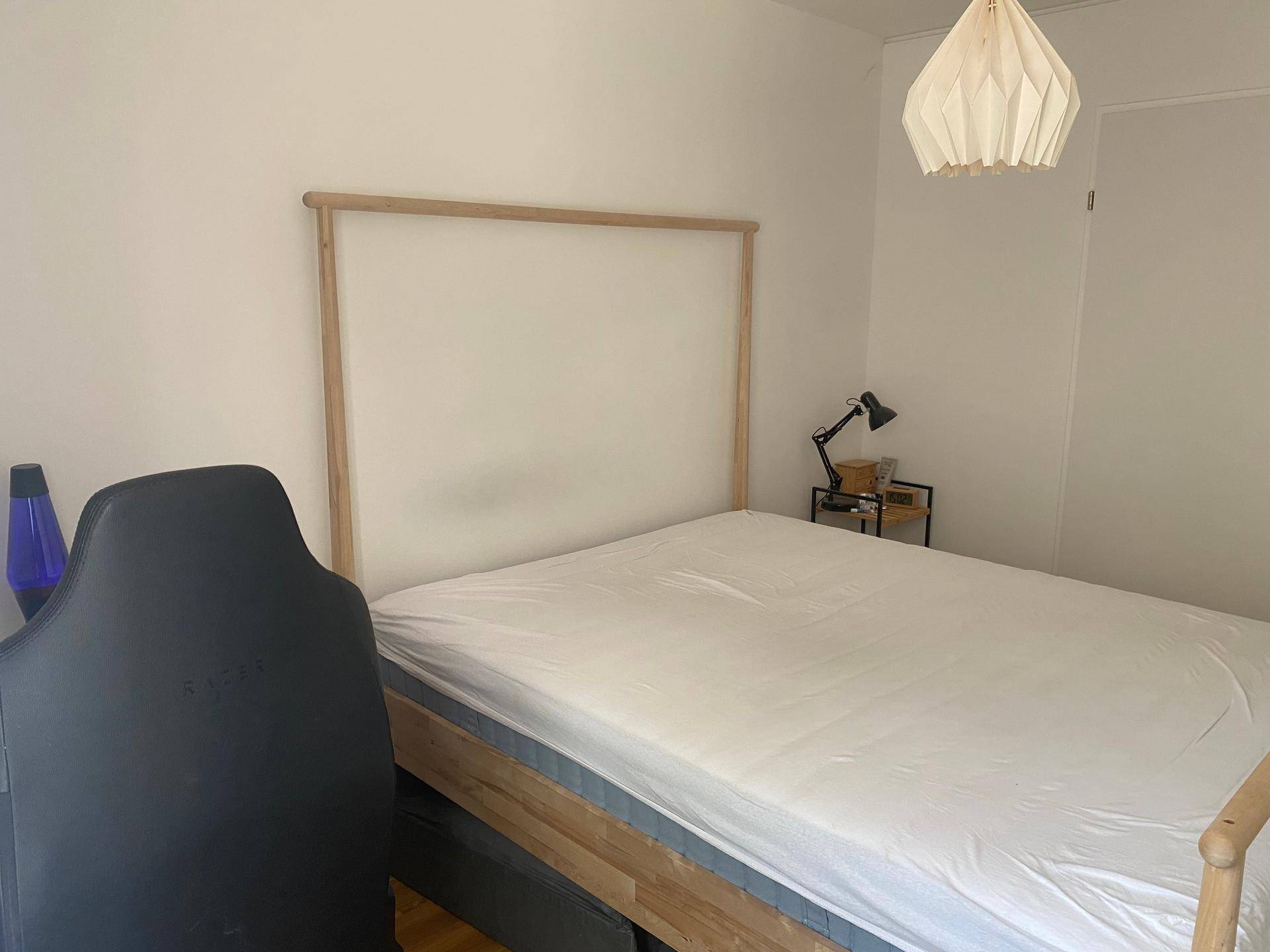 Schlafzimmer mit hellem Holzbettrahmen, weißer Bettwäsche und modernem Deckenlicht.