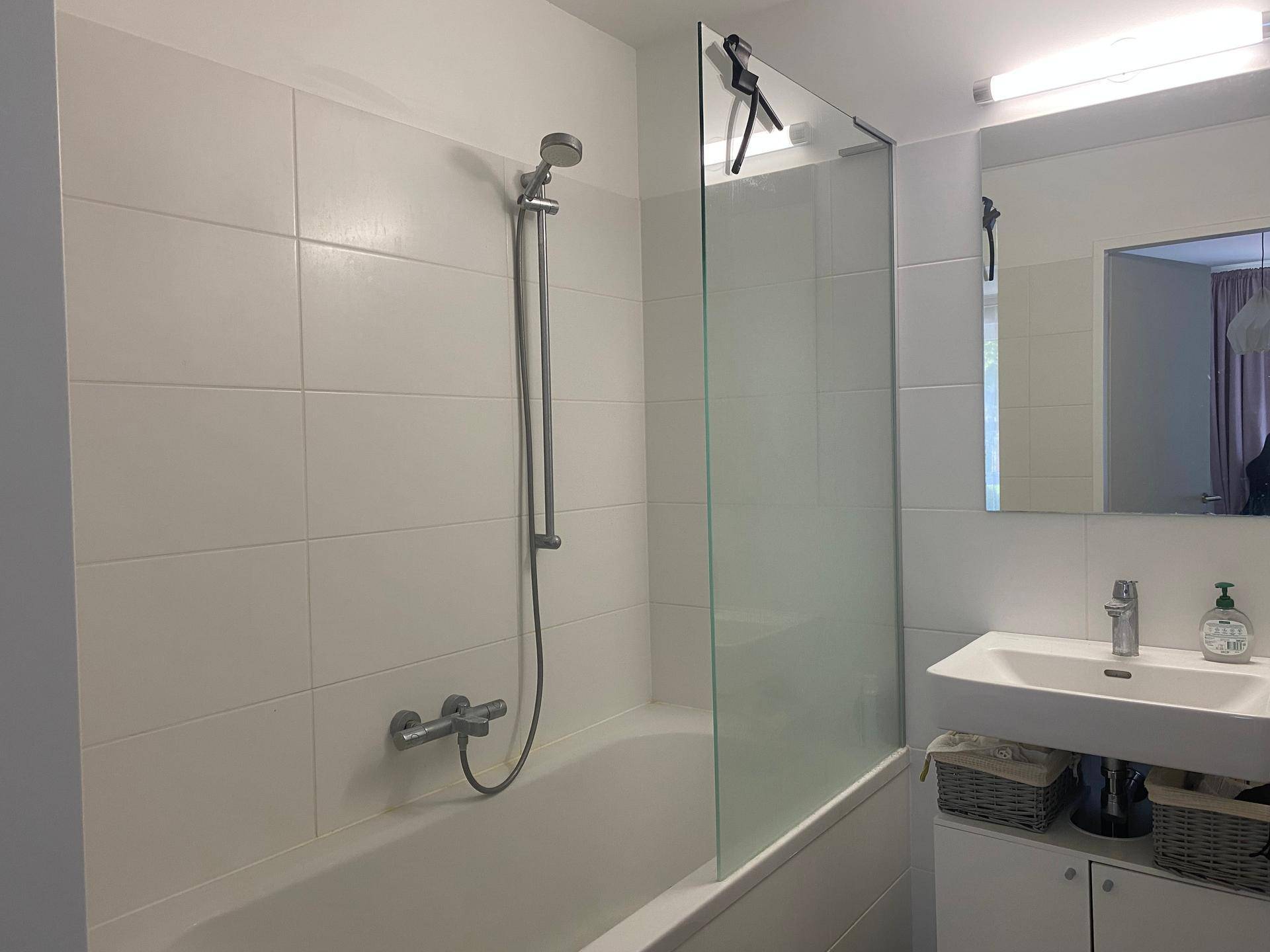 Helles Badezimmer mit Badewanne, Duschvorrichtung, Einzelwaschbecken und weißen Fliesen.