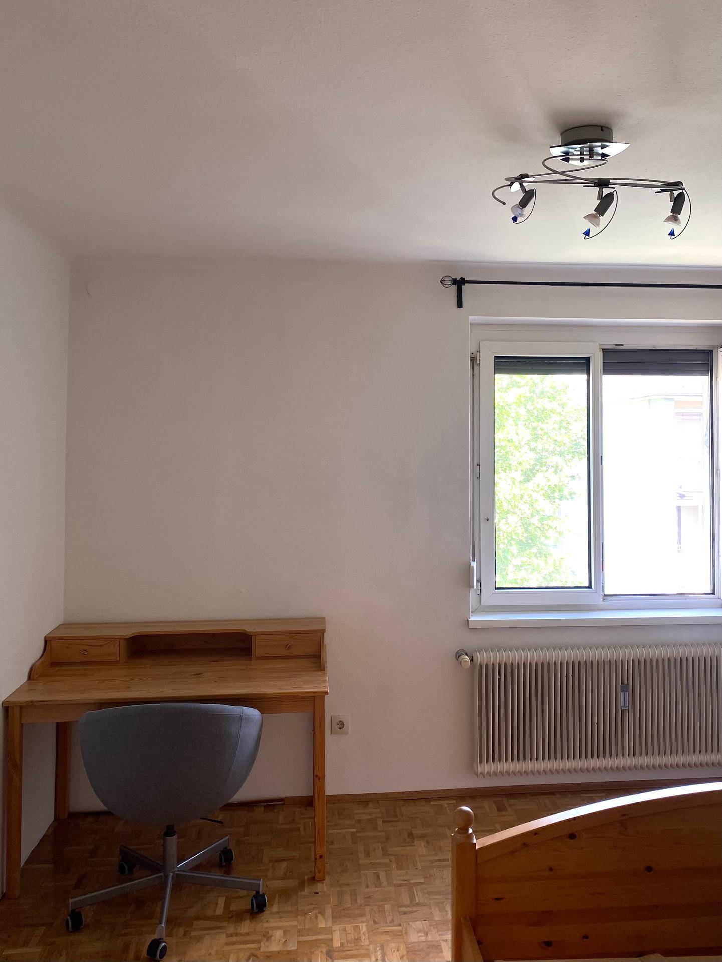 Helles Schlafzimmer mit Holzschreibtisch, Parkettboden und Fensterblick ins Grüne.