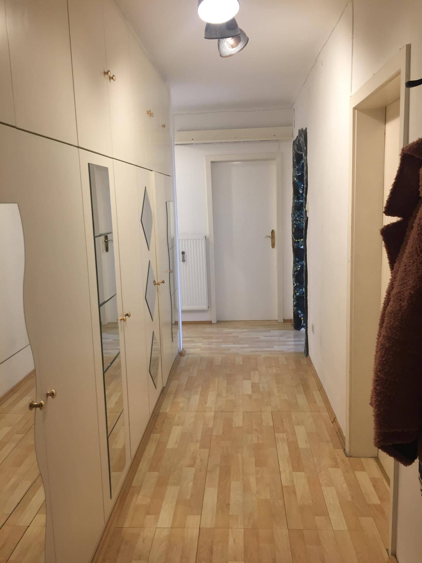 Langer Flur mit Einbauschränken, Spiegelfronten und hellem Laminatboden.