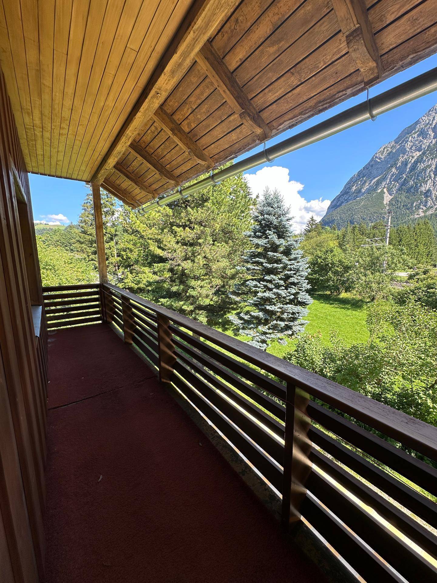 Überdachter Holzbalkon mit Bergblick und grüner Umgebung, ideal zum Entspannen.