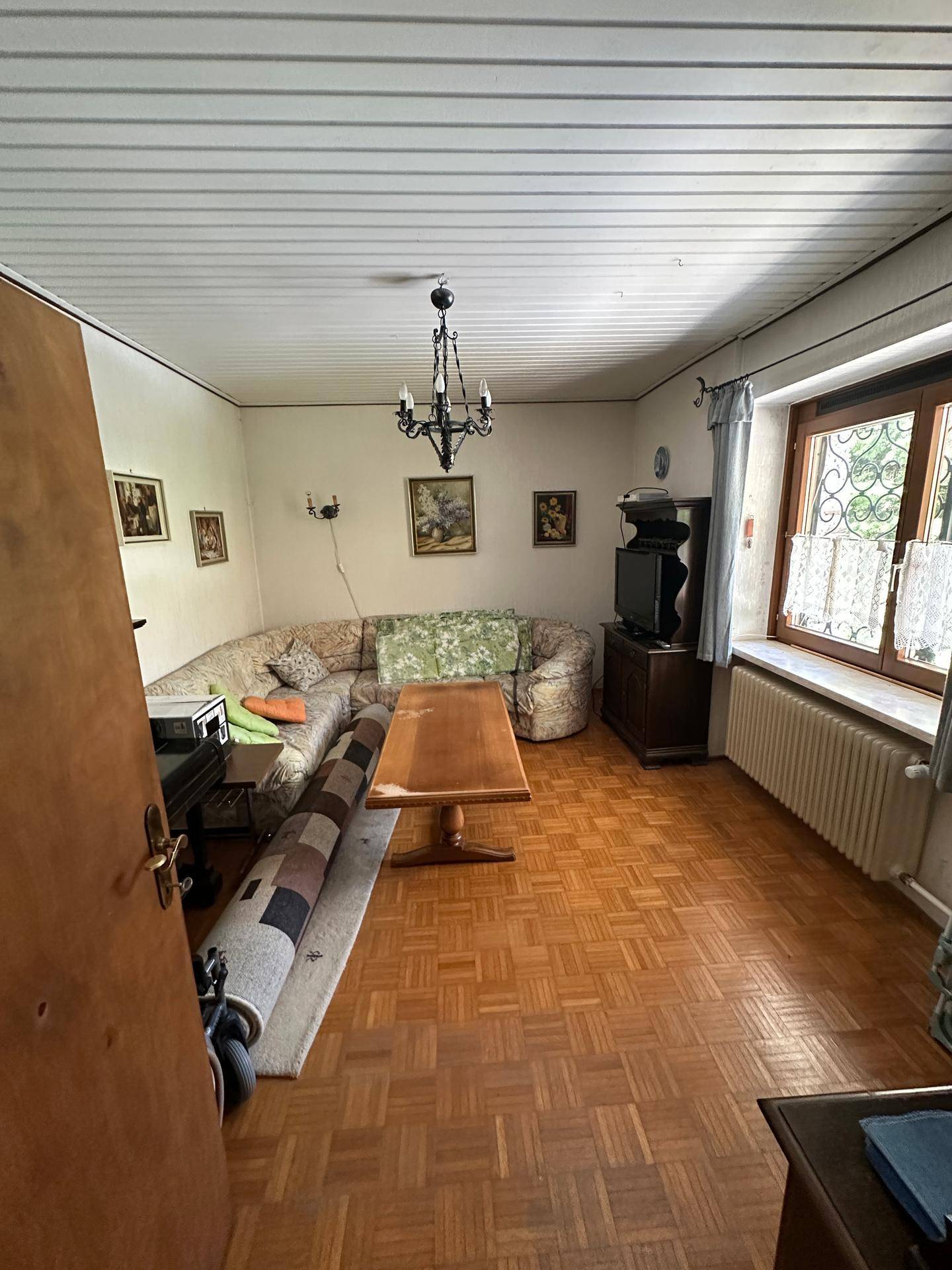 Gemütliches Wohnzimmer mit Holzparkett, Ecksofa und traditionellem Kronleuchter.